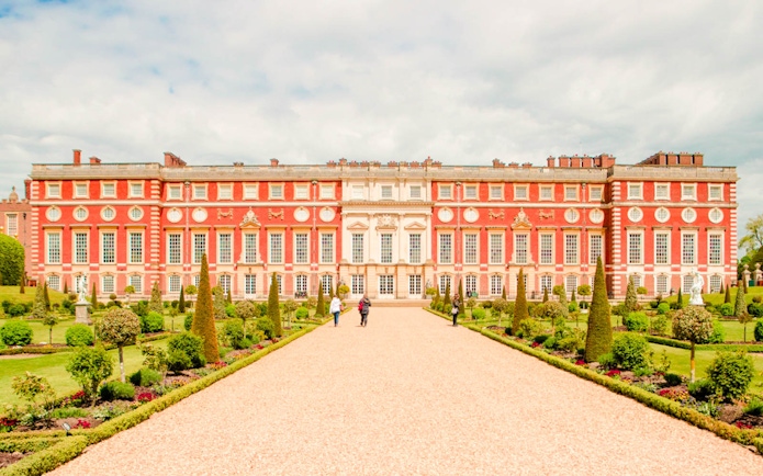 Hampton Court Palace facade with gardens and visitors in London.