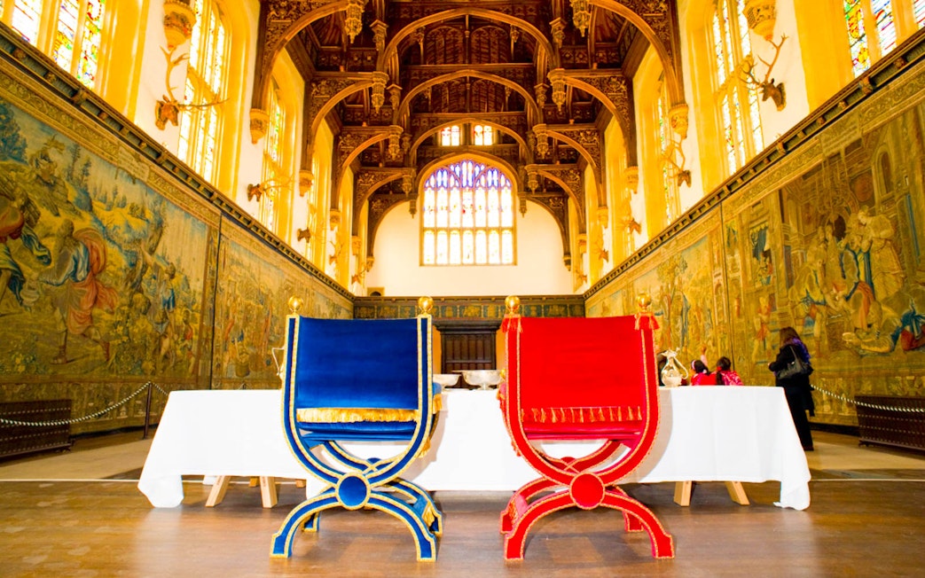Visitors inside the Great Hall of Hampton Court Palace, London, viewing historic tapestries.