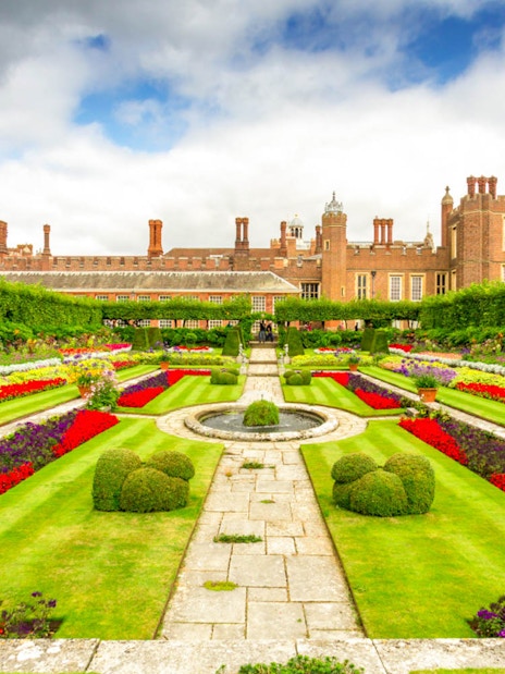 Hampton Court Palace gardens with colorful flower beds and historic architecture in the background.