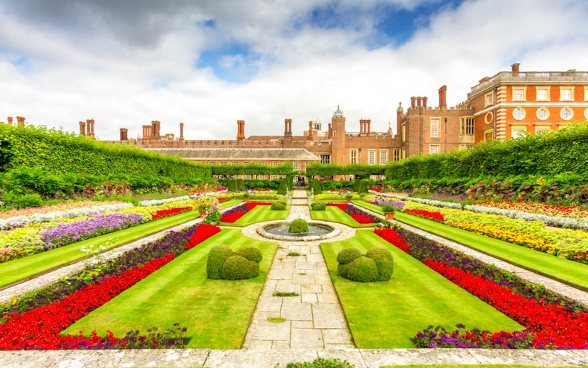 Hampton Court Palace gardens with colorful flower beds and historic architecture in the background.