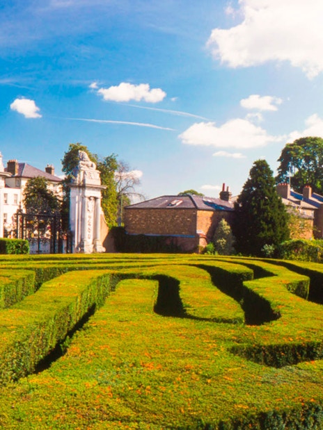 Hampton Court Palace garden maze with historic buildings in the background.