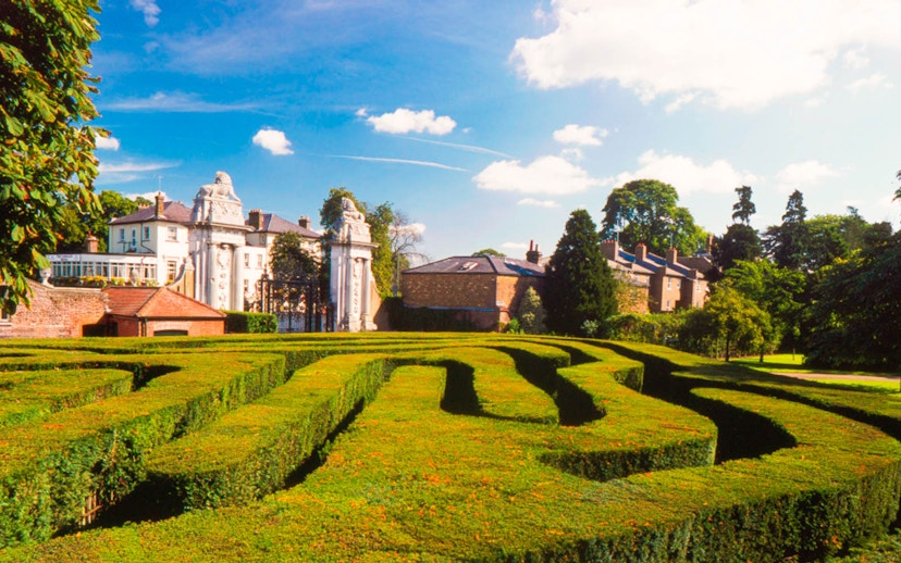 Hampton Court Palace garden maze with historic buildings in the background.
