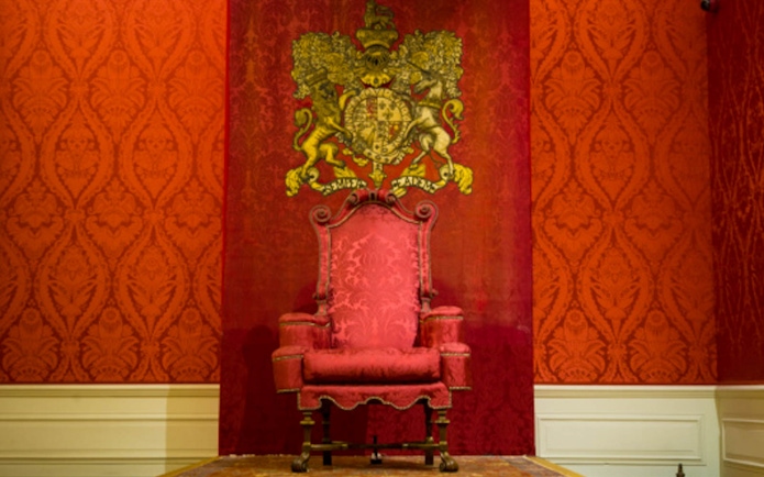 Throne room with ornate red chair and royal crest at Hampton Court Palace.
