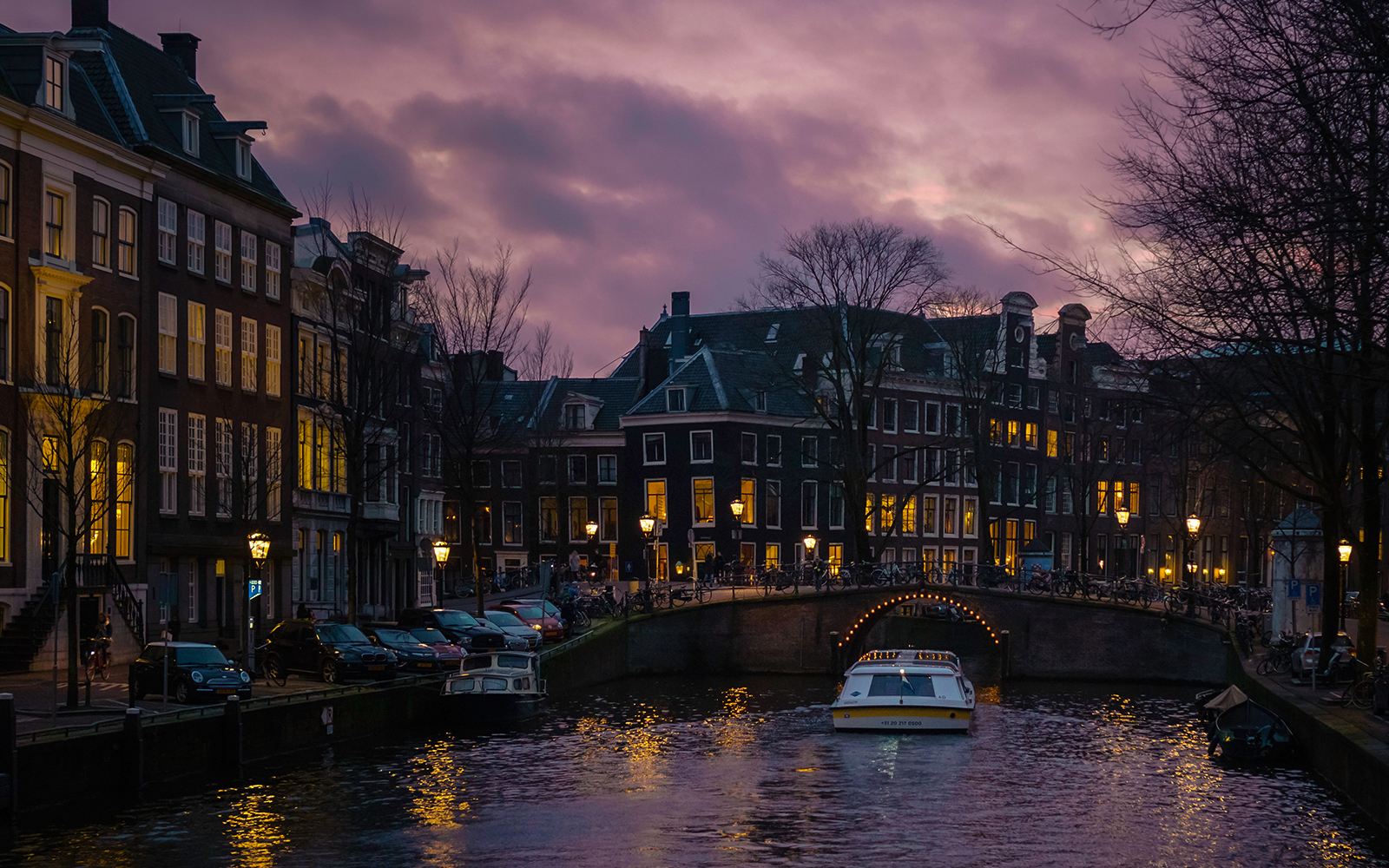Canal cruise at dusk in Amsterdam with lit bridge and buildings.