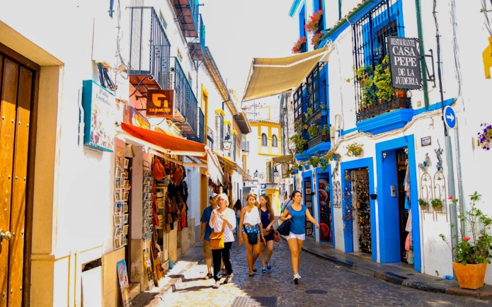 Narrow street in Cordoba with tourists walking, colorful buildings, and local shops.
