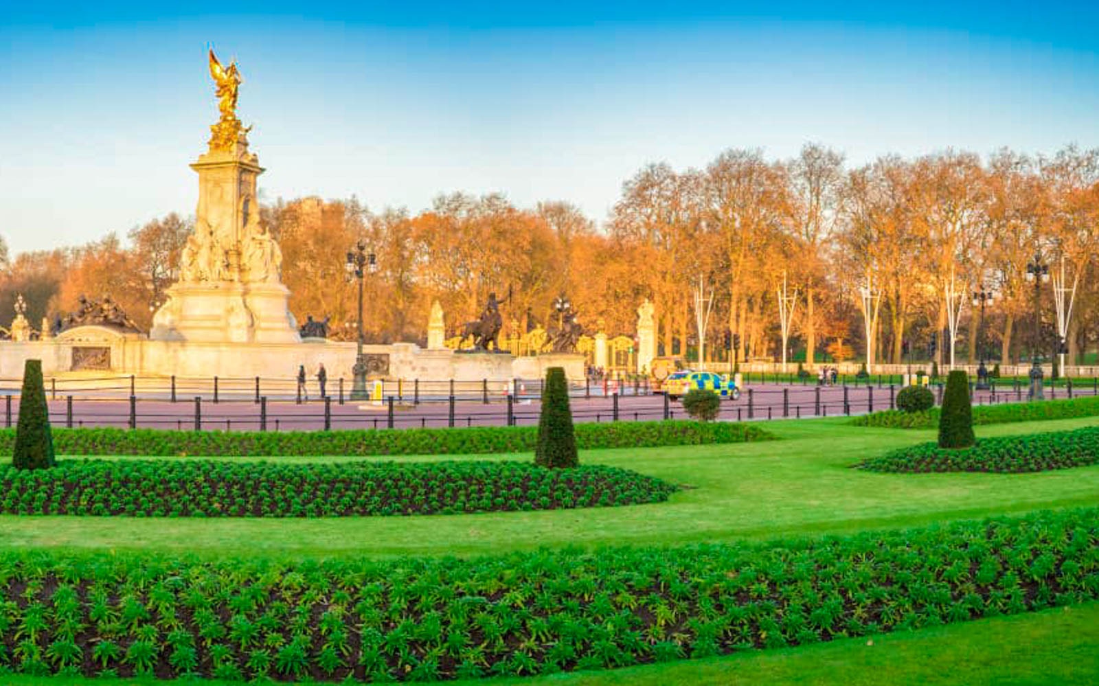 Victoria Memorial in front of Buckingham Palace, London, with manicured gardens and autumn trees.