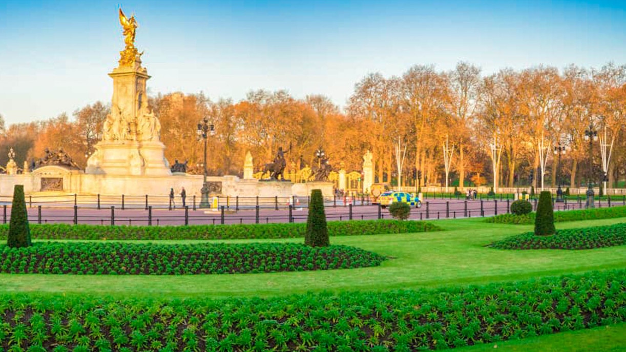 Victoria Memorial in front of Buckingham Palace, London, with manicured gardens and autumn trees.