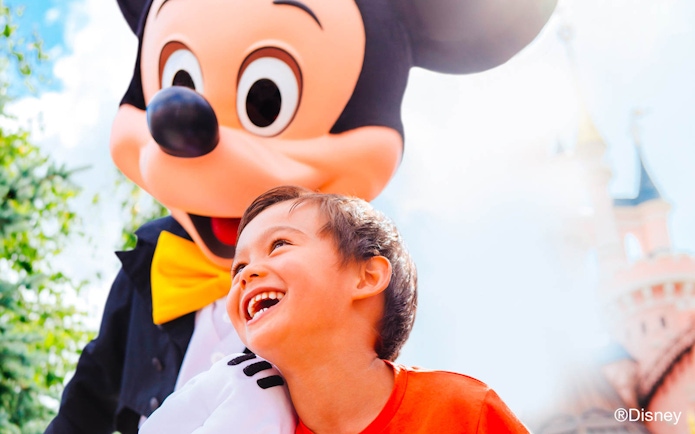 Child smiling with a character at Disneyland Paris, castle in background.