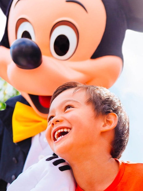 Child smiling with a character at Disneyland Paris, castle in background.