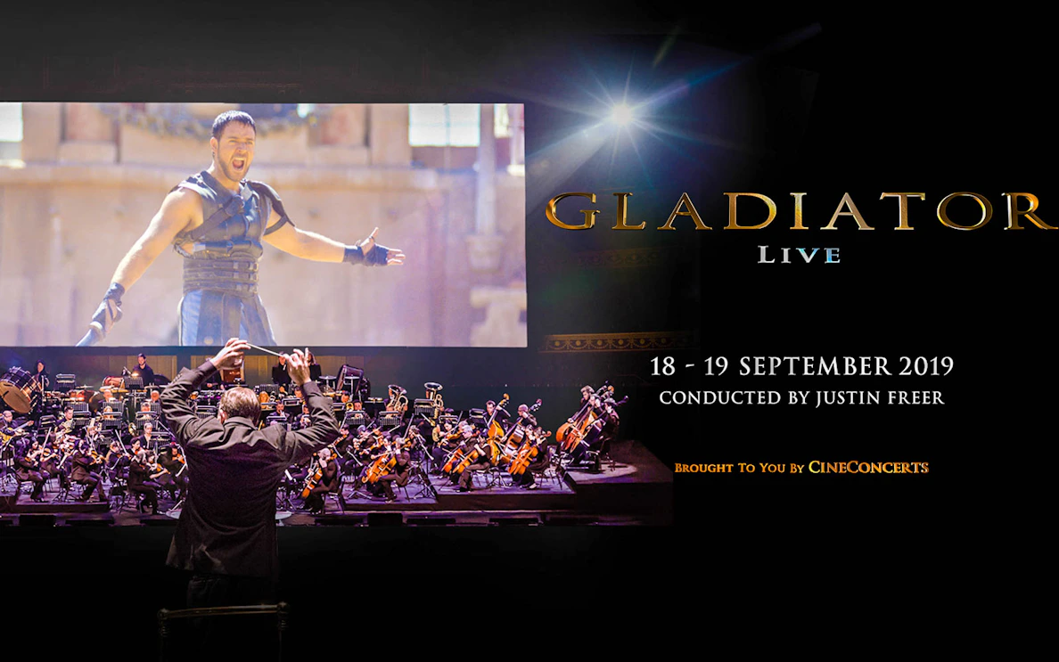 Conductor leading orchestra for Gladiator Live in Concert with film scene displayed.