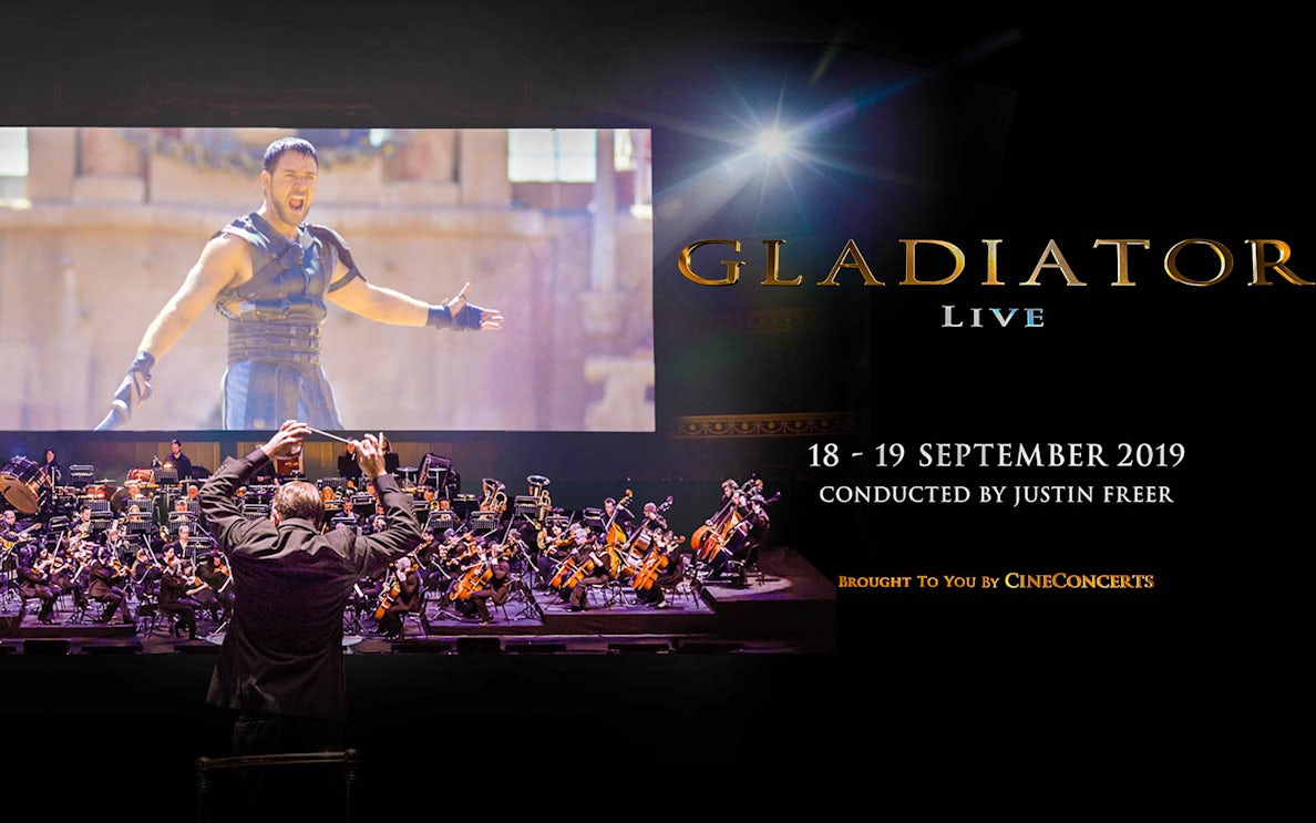 Conductor leading orchestra for Gladiator Live in Concert with film scene displayed.