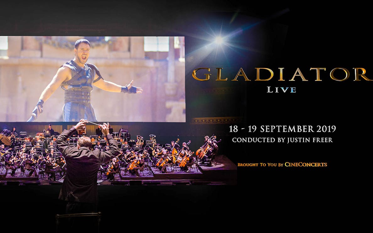 Conductor leading orchestra for Gladiator Live in Concert with film scene displayed.