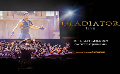 Conductor leading orchestra for Gladiator Live in Concert with film scene displayed.
