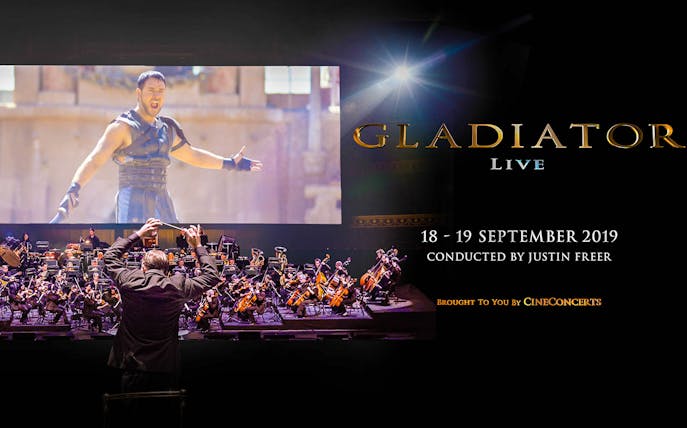 Conductor leading orchestra for Gladiator Live in Concert with film scene displayed.