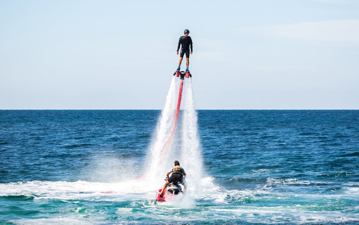 Person flyboarding over ocean with jet ski in background.