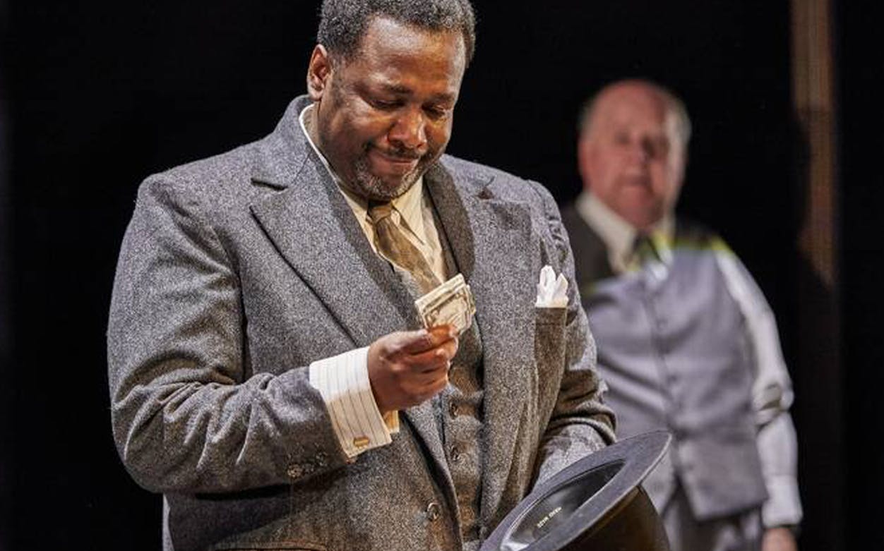 Man in suit holding money, scene from "Death of a Salesman" play.