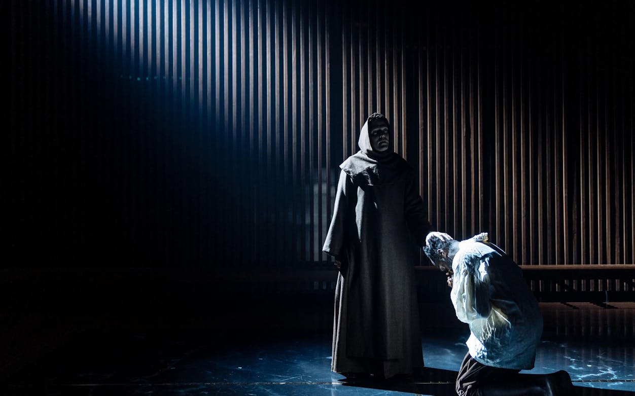 Two actors perform a dramatic scene from "Measure for Measure" on a dimly lit stage.