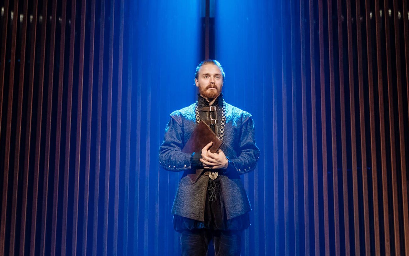 Actor in period costume holding a book on stage during "Measure for Measure" performance.