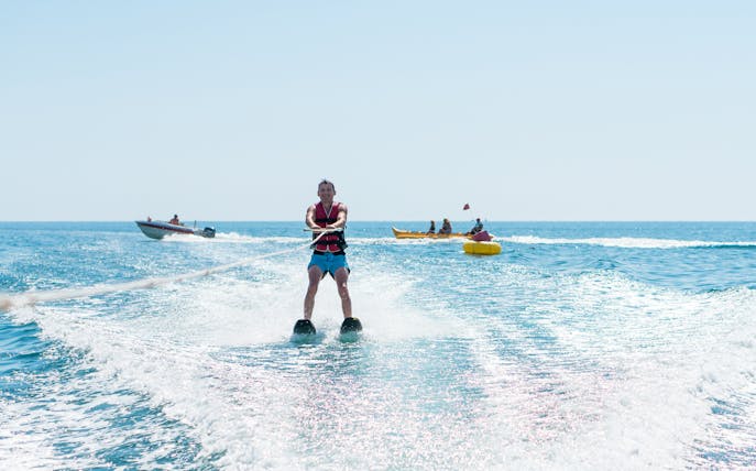Water skiing on open sea with boats in the background.