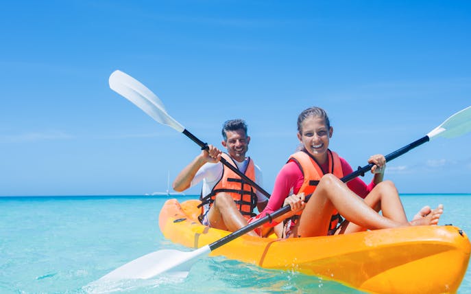 Two people kayaking in clear blue waters wearing life vests.