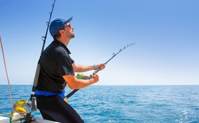 Man deep sea fishing on a boat in open ocean.
