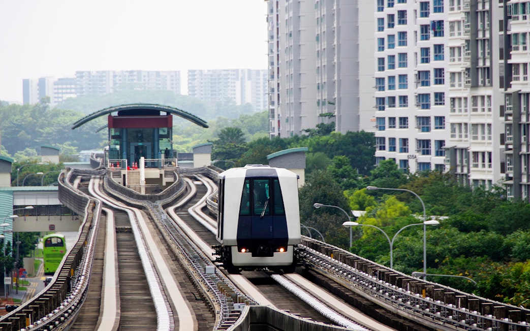 Singapore MRT train approaching a station, surrounded by residential buildings and greenery.