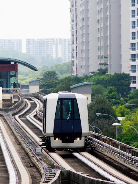 Singapore MRT train approaching a station, surrounded by residential buildings and greenery.