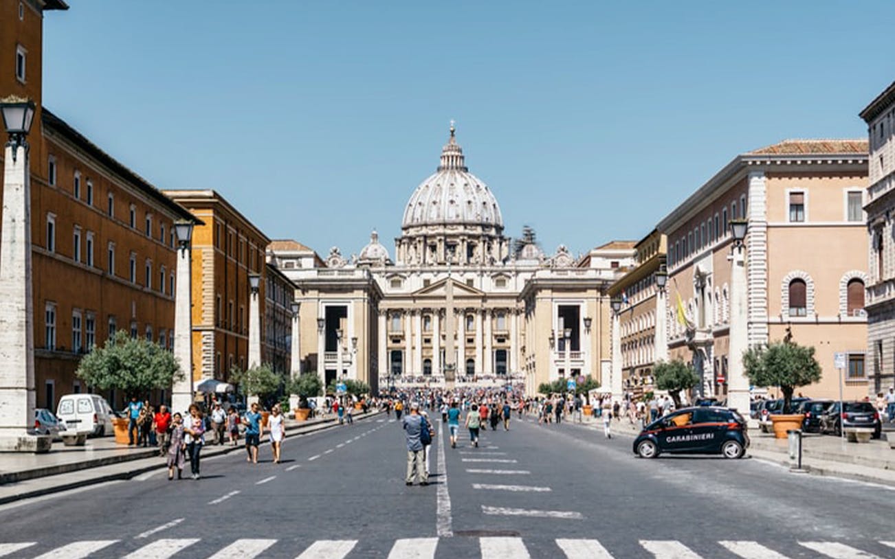 St. Peter’s Basilica exterior with tourists walking in Vatican City.