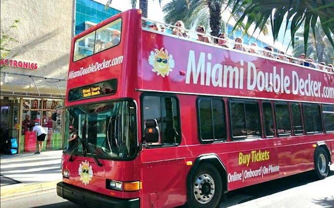 Red double-decker bus on Miami street with tourists on top deck.
