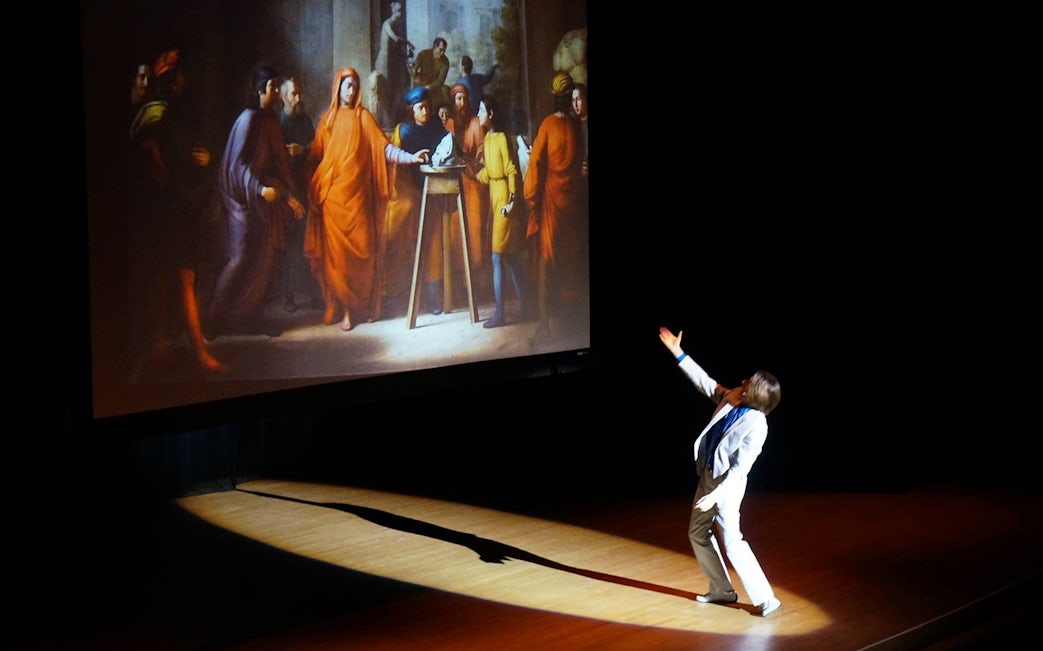 Performer gesturing towards a projected Renaissance painting during DaVinci and Michelangelo: The Titans Experience.