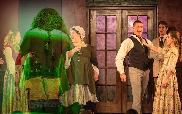 Theatrical scene with actors in period costumes and a green-lit figure, related to Frankenstein.