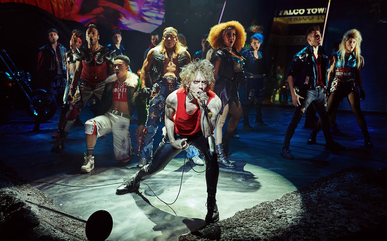 Performer singing on stage with a group in a scene from "Bat Out of Hell" musical.