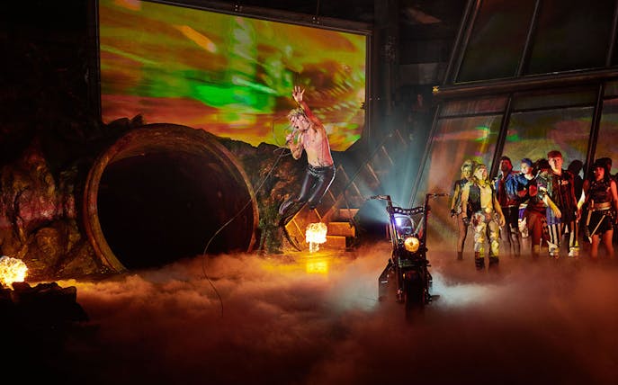 Performer leaping on stage with group and motorcycle in "Bat Out of Hell" show.
