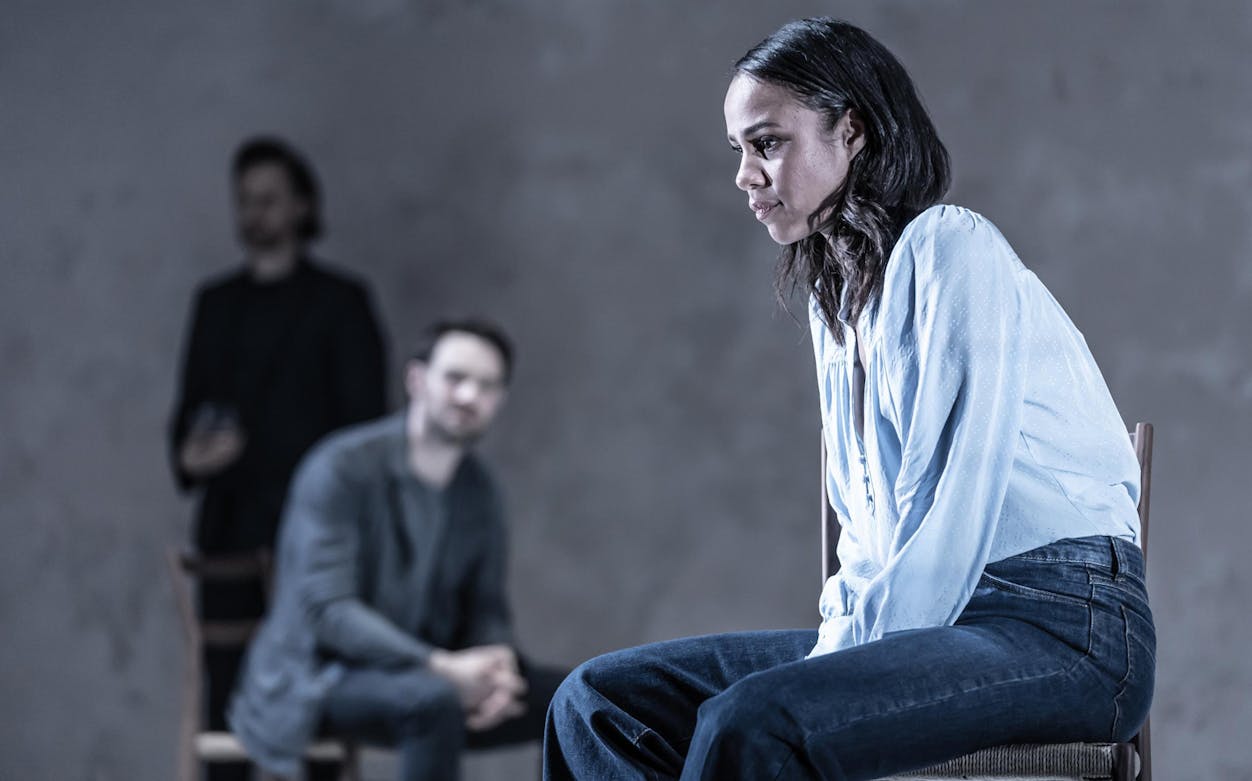 Woman sitting pensively with two blurred figures in the background, conveying betrayal theme.