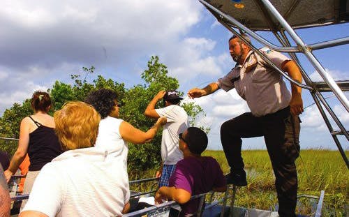 Everglades airboat tour guide pointing out wildlife to passengers.