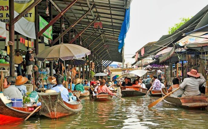 Boats navigating Damnoen Saduak Floating Market canal, Thailand.