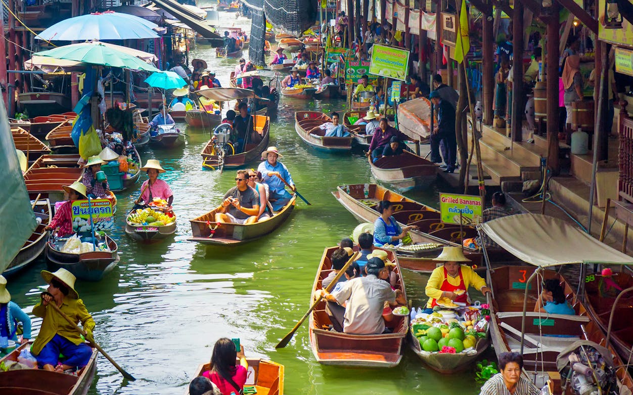 Damnoensaduak Floating Market boats with goods, River Kwai bridge in background, Bangkok, Thailand.