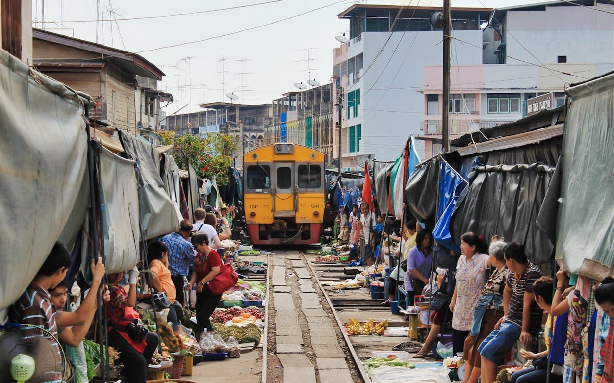 Train passing through Maeklong Train Market, Thailand, with vendors and goods on either side.