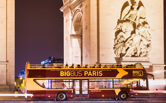 Big Bus tour passing by the Arc de Triomphe at night in Paris.
