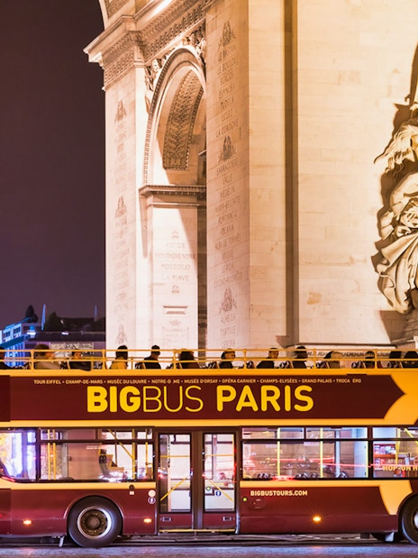 Big Bus tour passing by the Arc de Triomphe at night in Paris.