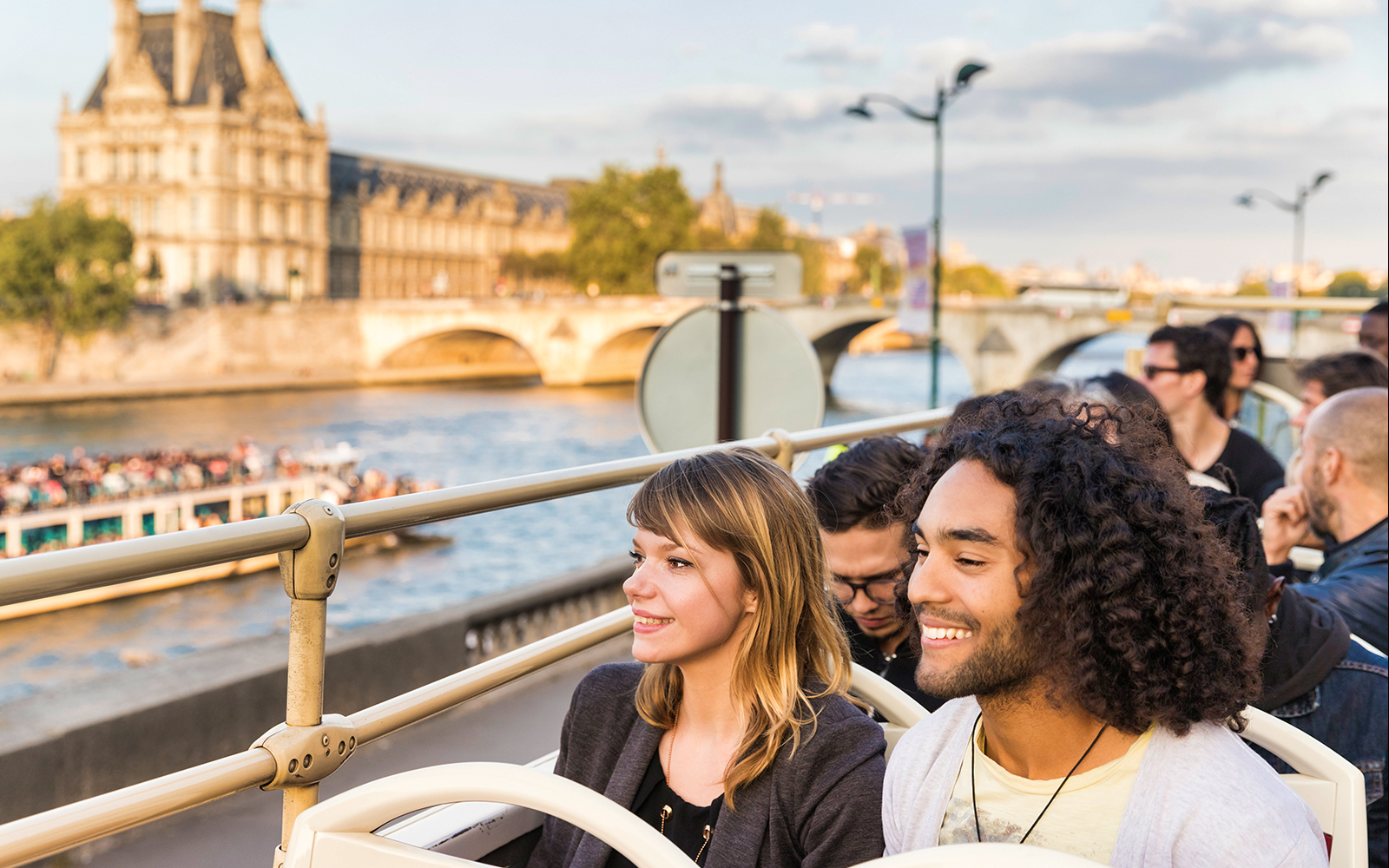 Open-top bus tour in Paris with view of Seine River and historic architecture.