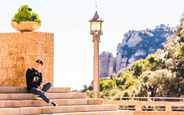 Person sitting on steps at Montserrat Monastery with mountain view in background.