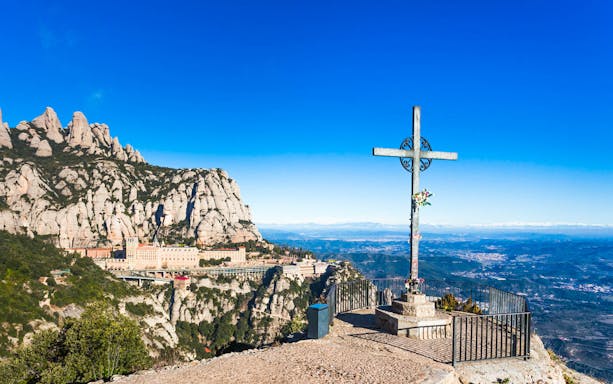 Montserrat Monastery with mountain backdrop and cross, Spain.