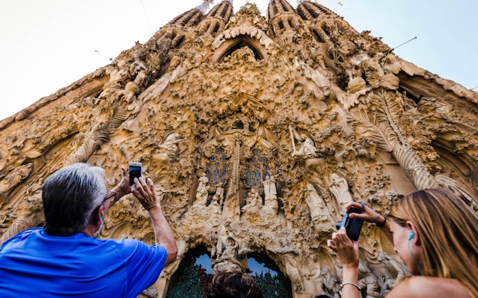 Sagrada Familia facade with tourists taking photos during guided tour in Barcelona.