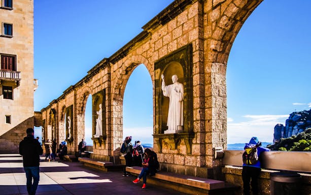 Visitors exploring Montserrat's stone arches and statues on a guided tour.