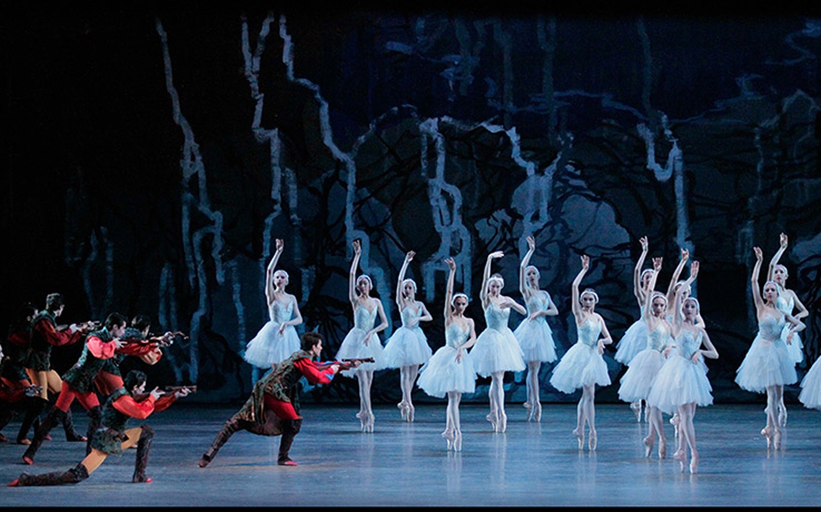 Ballet dancers performing Swan Lake on stage with a dark forest backdrop.