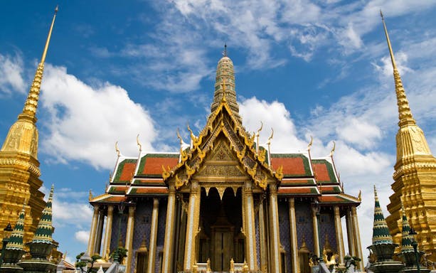 Ayutthaya temple with ornate golden spires under a blue sky, part of UNESCO tour from Bangkok.
