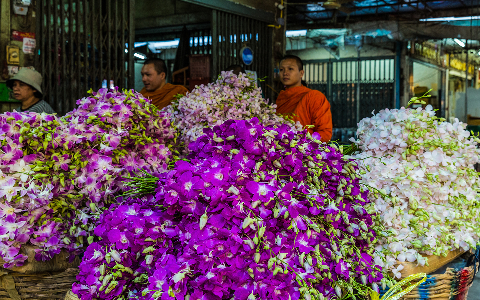 Flower market in Bangkok with vibrant orchids and monks in the background.
