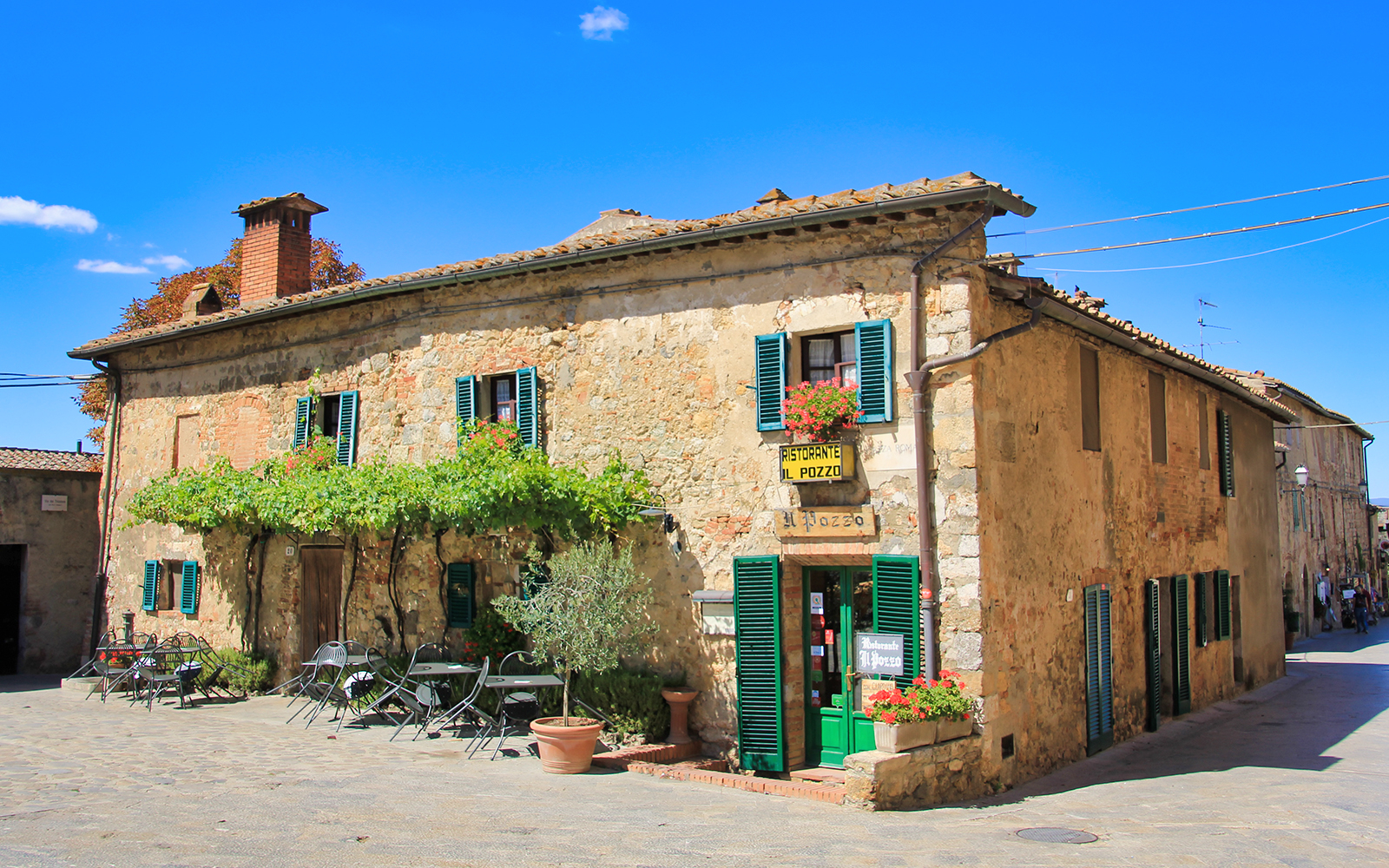 Stone building with green shutters and outdoor seating at a restaurant in Tuscany, Italy.