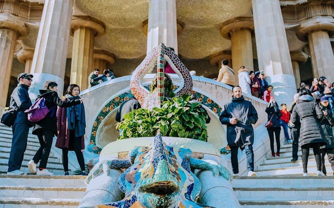 Visitors at Park Güell's mosaic lizard fountain, Barcelona, during guided tour.